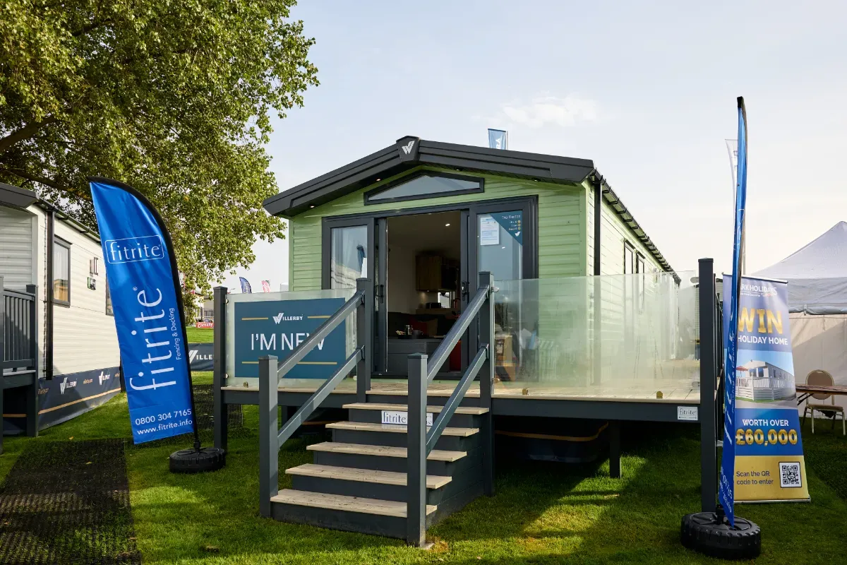 A Willerby Buxton premium mid-range holiday home. It features green cladding, light coloured decking and has a window above the sliding French doors for extra light.