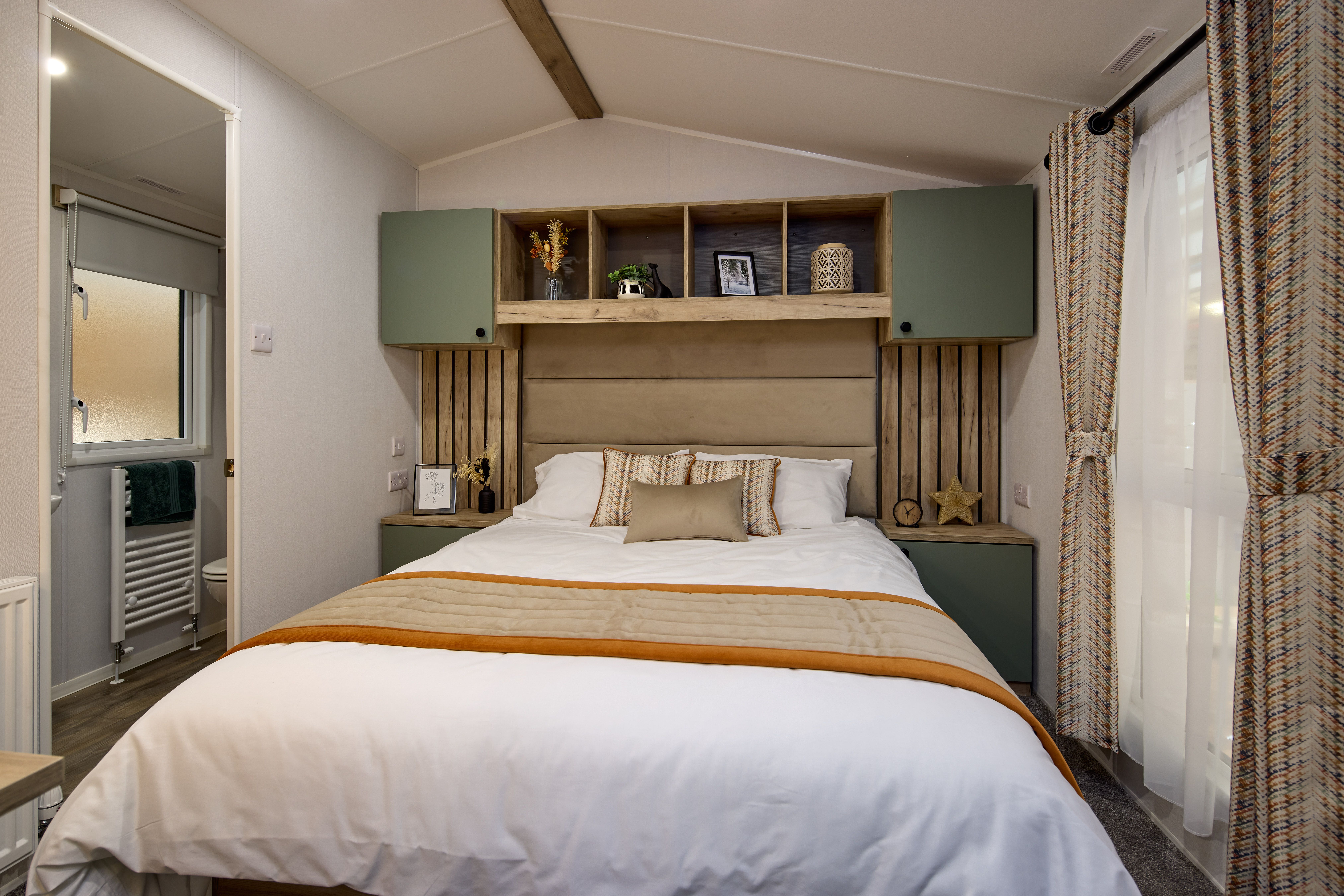 The master bedroom in the Willerby Buxton holiday home. The en-suite bathroom can be glimpsed through a side door. The bed is large and built-in cupboards provide plenty of storage. Full-height windows let in plenty of light. 
