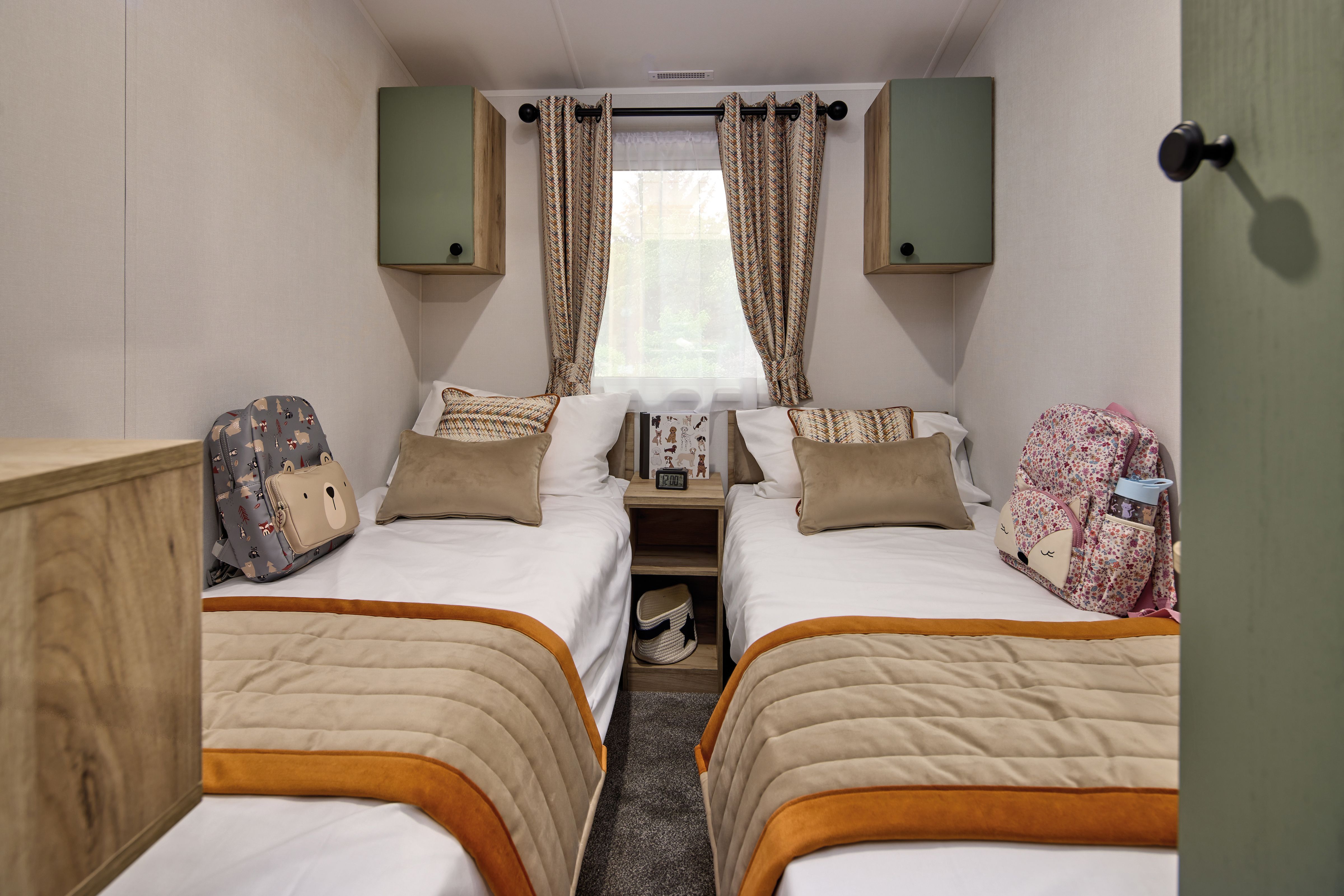 A twin bedroom in the Willerby Buxton holiday home. Two single beds have red throws to contrast with the green and cream colour scheme. A large window lets in plenty of light. 