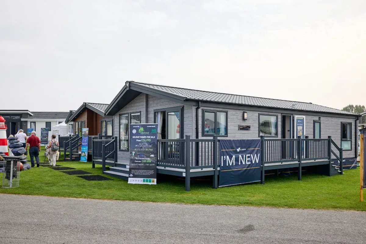 A Willerby New Holland premium lodge. It is wider than a standard holiday home and features light grey cladding and large windows on the front. 