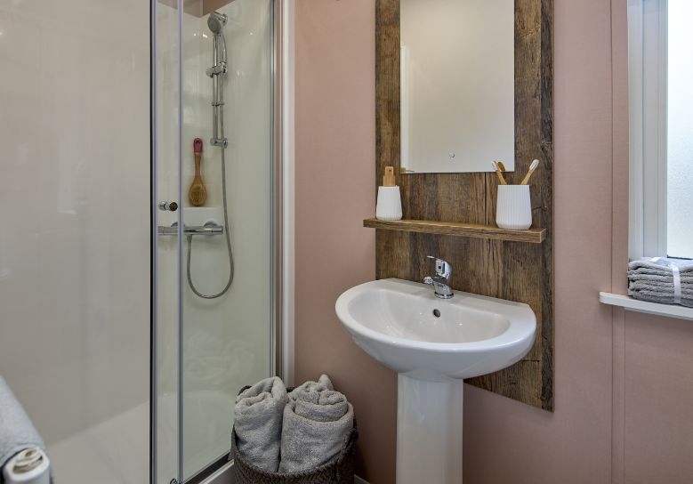 The Willerby Malton Elite ensuite bathroom has a pink accent wall with dark oak effect units which match the colour scheme of the home.