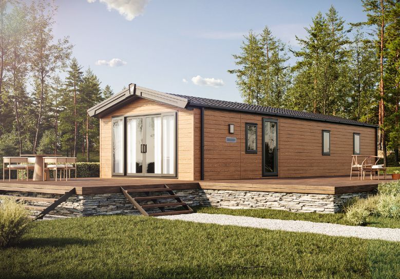 The Willerby Malton Elite in Brown sited on a stone and wooden decking in a secluded forest.