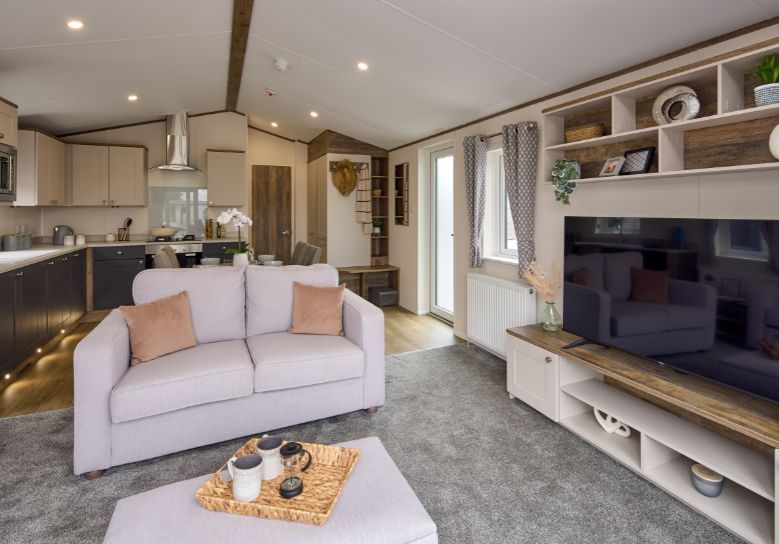 The Willerby Malton Elite spacious lounge with two grey free-standing sofas and a matching footstool with a storage media unit in cream and a dark oak effect.