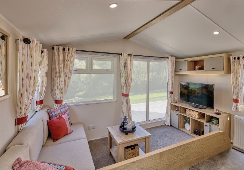 The Willerby Rio lounge has a fixed grey corner sofa with an optional orange armchair, and has a oak effect media unit with light grey cupboard doors with a matching coffee table.