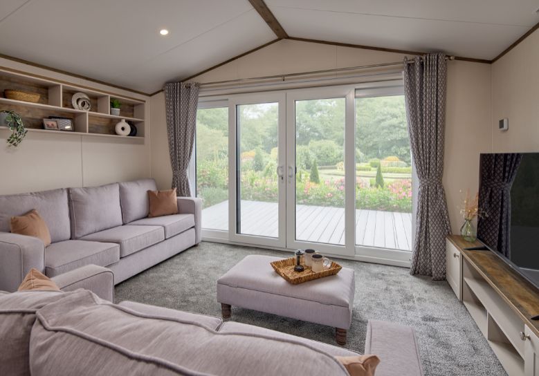 The Willerby Malton Elite spacious lounge with two grey free-standing sofas and a matching footstool with a storage media unit in cream and a dark oak effect.