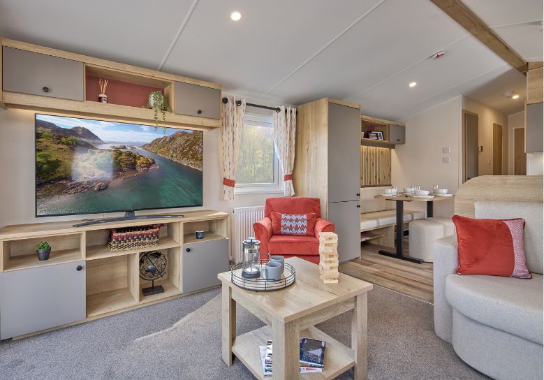 The Willerby Rio lounge has a fixed cream corner sofa with an optional orange armchair, and has a oak effect media unit with light grey cupboard doors with a matching coffee table.