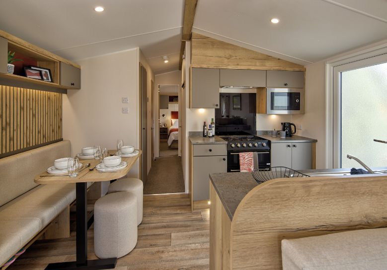 The Willerby Rio kitchen and dining area has oak effect kitchen storage units with light grey cupboards and worktops, and the dining area has an oak effect acoustic accent wall.