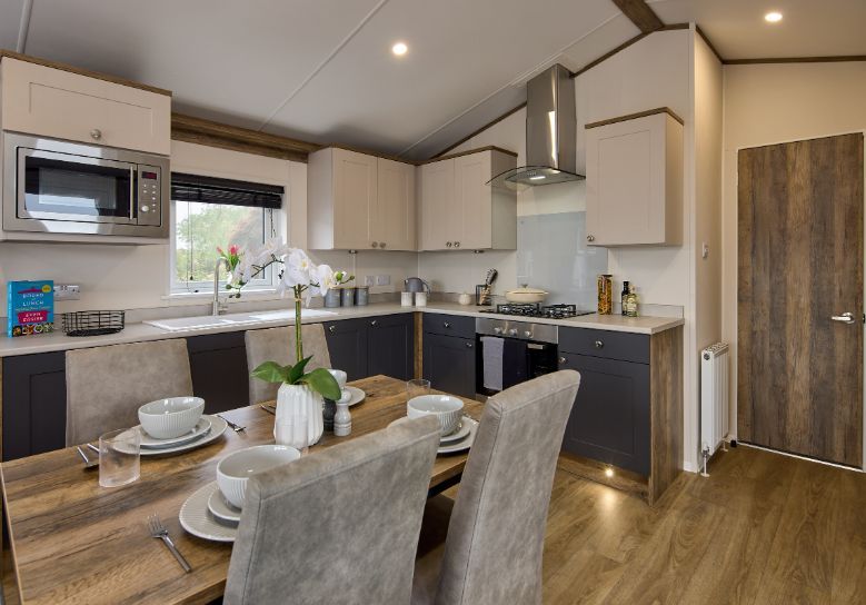 The Willerby Malton Elite kitchen has a dark oak effect dining table with grey seating, and dark grey and cream cupboard doors matching the homes colour scheme.