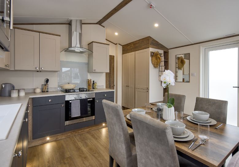 The Willerby Malton Elite kitchen has a dark oak effect dining table with grey seating, and dark grey and cream cupboard doors matching the homes colour scheme.