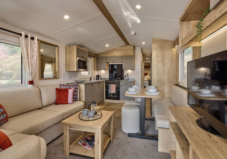 The Willerby Rio Compact lounge has a fixed cream corner sofa , and has a oak effect media unit with light grey cupboard doors with a matching coffee table.