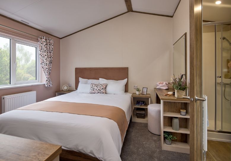 The Willerby Malton Elite master bedroom has a pink accent wall, matching the headboard of the bed, and has a storage dressing table in dark oak effect.