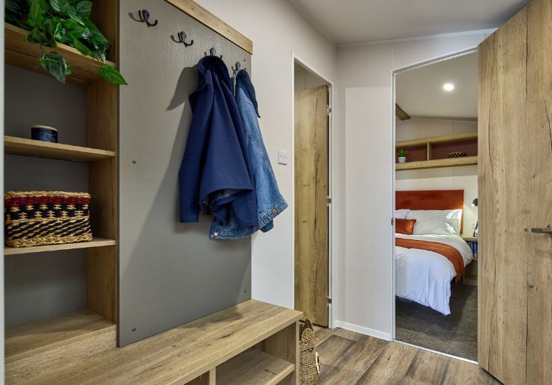 The Willerby Rio Compact entrance has a oak effect and grey storage unit that doubles as seating, with hooks to hang up coats.