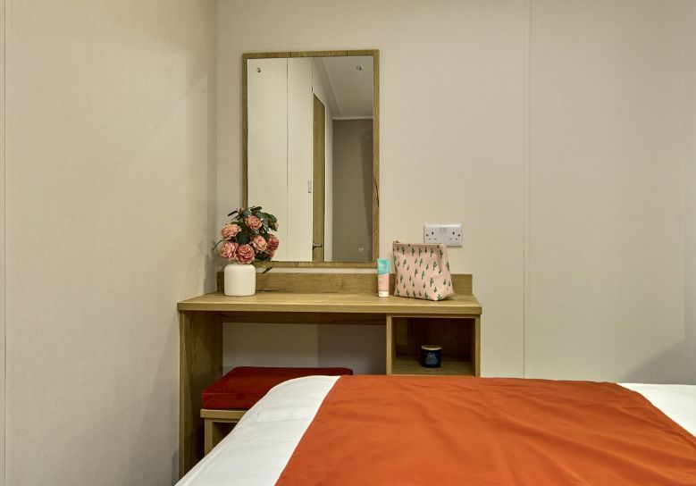 The Willerby Rio Compact master bedroom has dressing table in an oak effect with storage and an upholstered orange chair which matches the colour of the home.