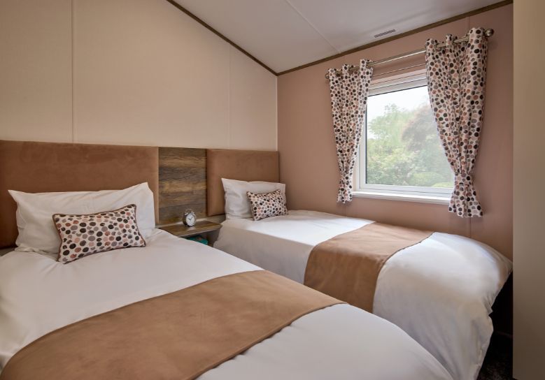 The Willerby Malton Elite twin bedroom has a pink accent wall matching the soft furnishings as well as the headboard, with a dark oak and cream storage unit which matches the master bedroom.