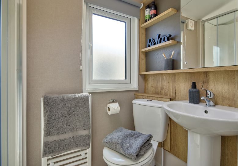 The Willerby Rio family shower room has oak effect storage units along the wall with a cream accent wall.