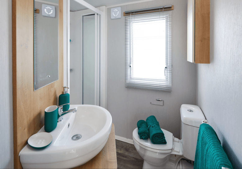 The Willerby Ashurst bathroom with oak effect units and green towels with a matching colour scheme soap dispenser set.