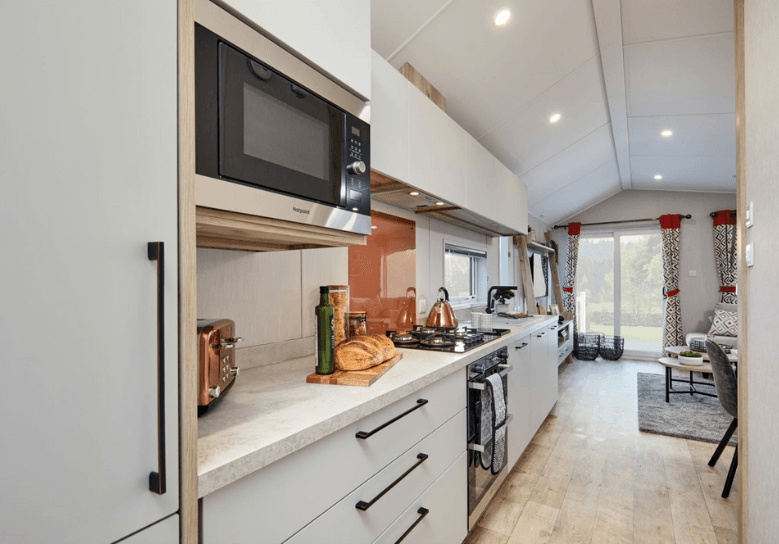 The Willerby Astoria stylish linear kitchen with white cupboard doors and an orange splashback.