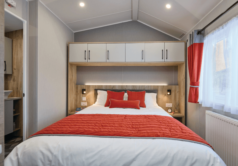 The Willerby Astoria master bedroom with an orange bedding set which matches the colour scheme, overhead oak effect storage and an ensuite bathroom connected.
