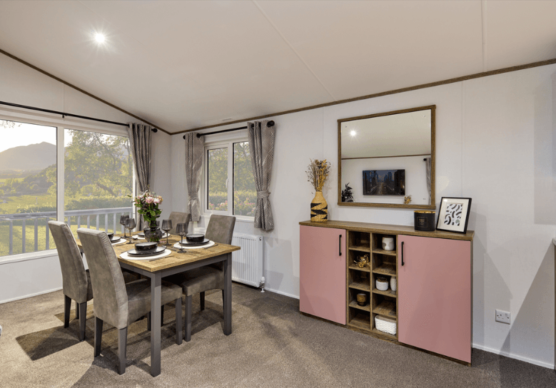 The Willerby Boston dining area with a storage unit to the right with blush pink cupboard doors and a large mirror.