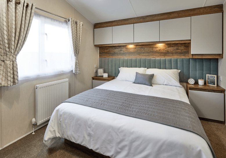 The Willerby Brookwood calming master bedroom with overhead storage with white cupboard doors and an upholstered sage green headboard.