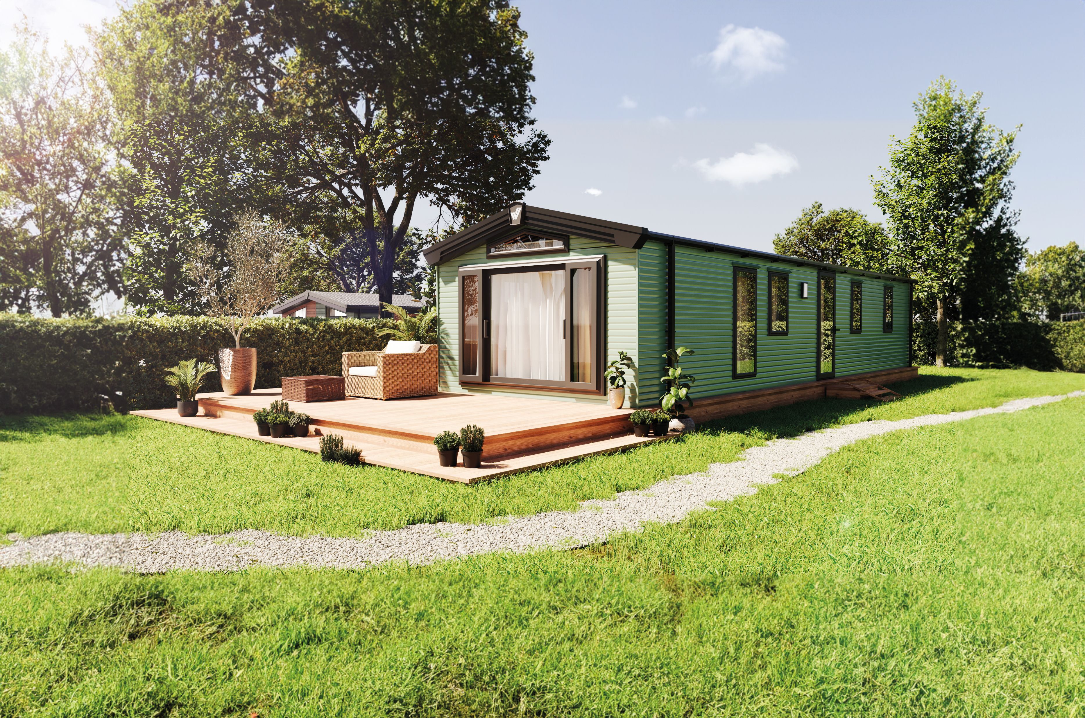 The Willerby Buxton holiday home on a grassy park with wooden decking. It has large windows at the front and is clad in a stylish sage green colour. 