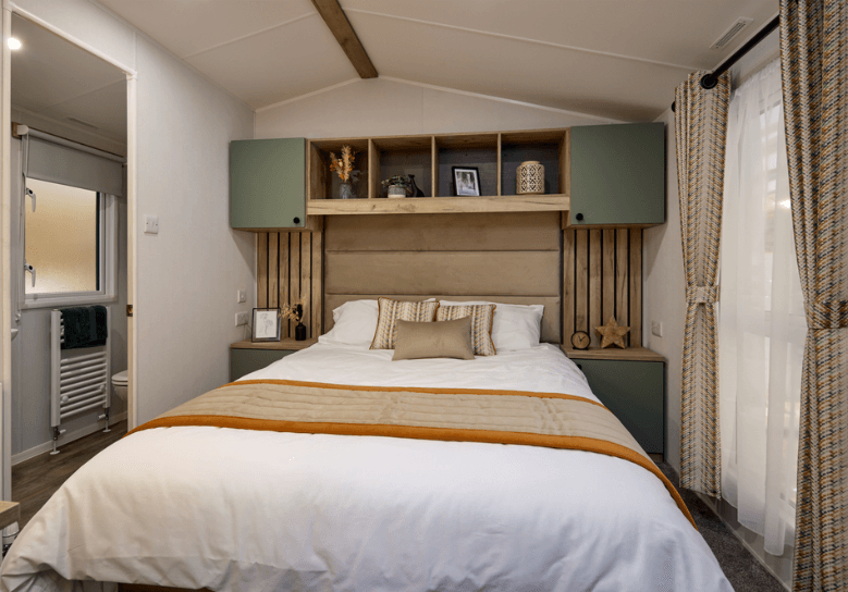 The Willerby Buxton stylish master bedroom with overhead storage and green cupboard doors and oak wood effect feature panelling.