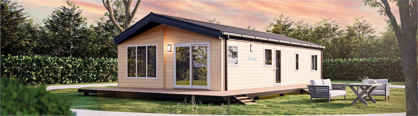 The Willerby Clearwater exterior is in a creamy yellow with a brown decking surrounding it. The Lodge is placed on a grassy field surrounded by bushes.