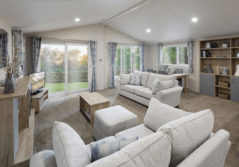 The Willerby Clearwater light and airy lounge with light grey sofas and a matching footstool, and oak effect storage units.