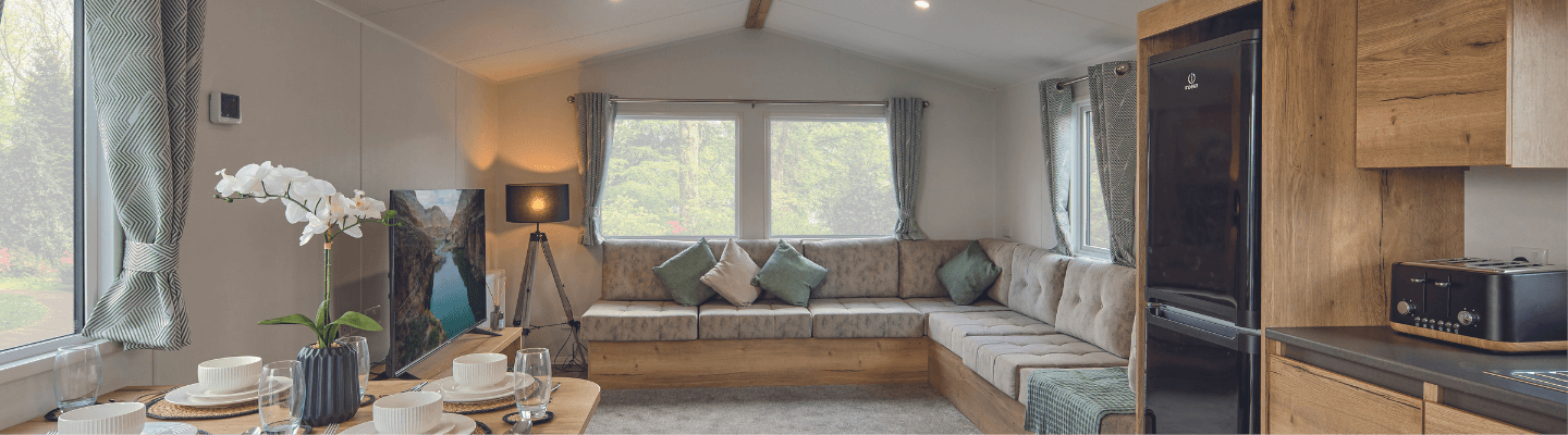 The Willerby Ellerton Extra lounge with fixed grey seating with soft green furnishings, and an overview of the oak effect units in the kitchen and dining area.