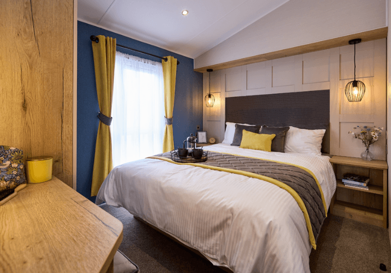 Gainsborough master bedroom with a blue accent wall, a panelled wall and yellow and grey soft furnishings.