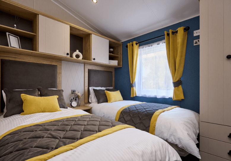 Gainsborough twin bedroom with grey and yellow soft furnishings, with a blue accent wall and overhead storage.