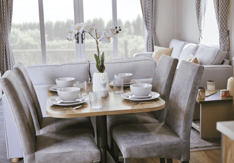 Malton dining area with 4 grey chairs and an oak table with white crockery and a centerpiece.