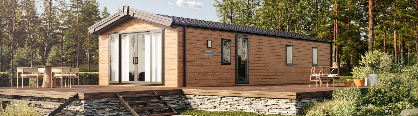 The Willerby Malton Elite in Brown sited on a stone and wooden decking in a secluded forest.