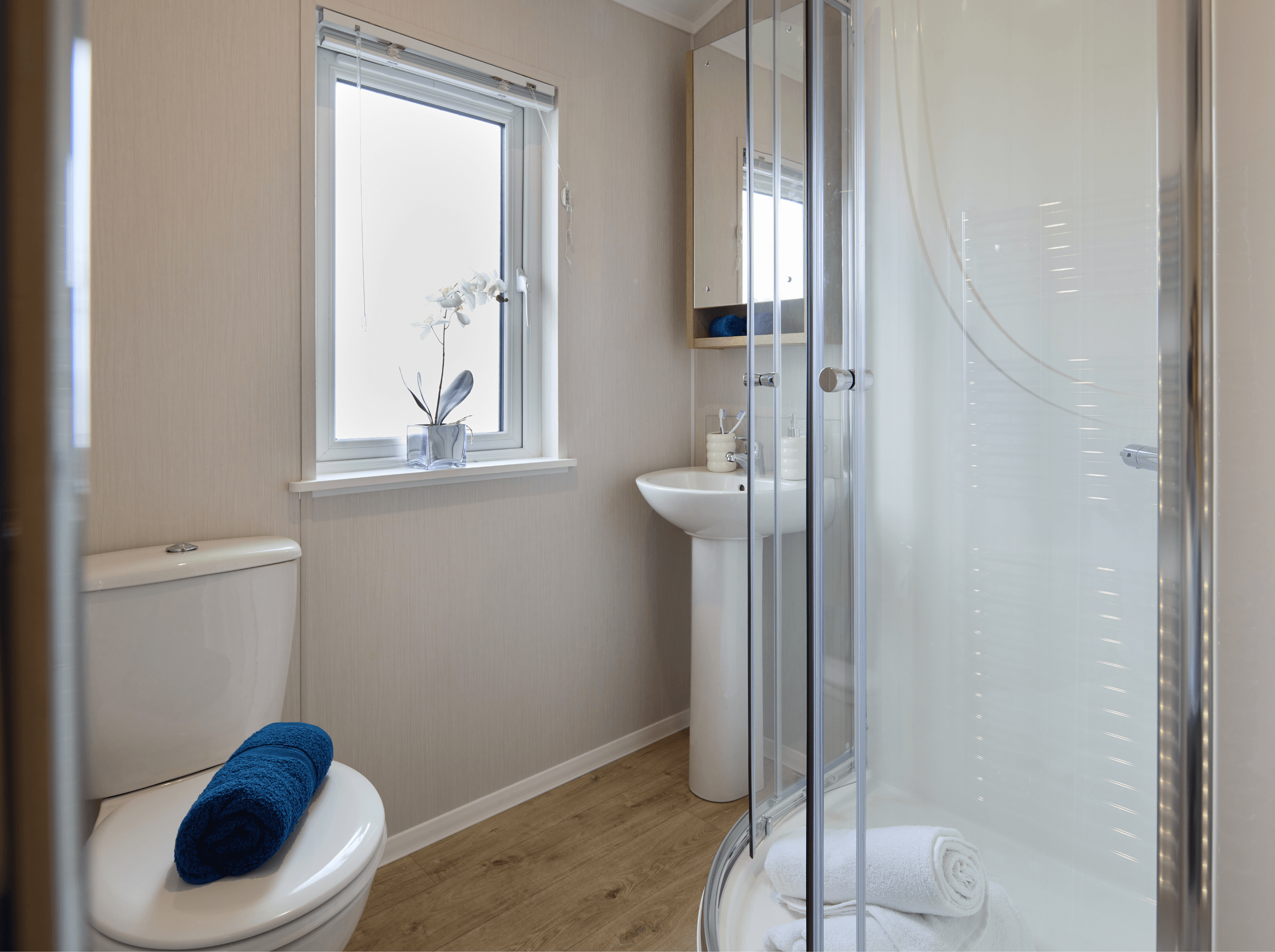 The en-suite bathroom in the Willerby New Holland holiday lodge. There is a shower cubicle and sink with a mirror unit above it. A large window lets light in. 