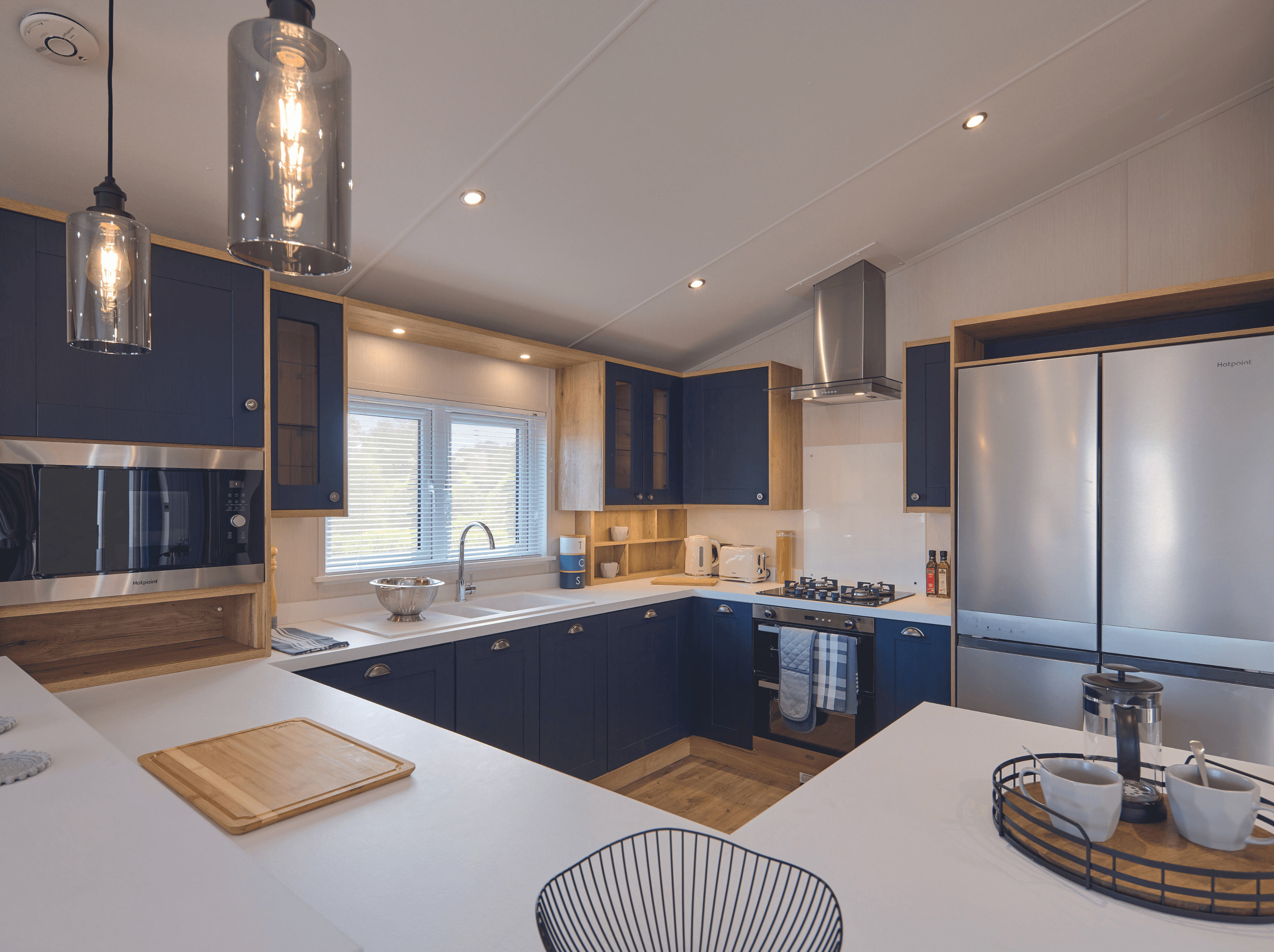 The kitchen of the Willerby New Holland holiday lodge. There is a large double fridge-freezer, fitted cooker and plenty of storage and worktop space. The colour scheme is stylish white and dark blue with wood features. 