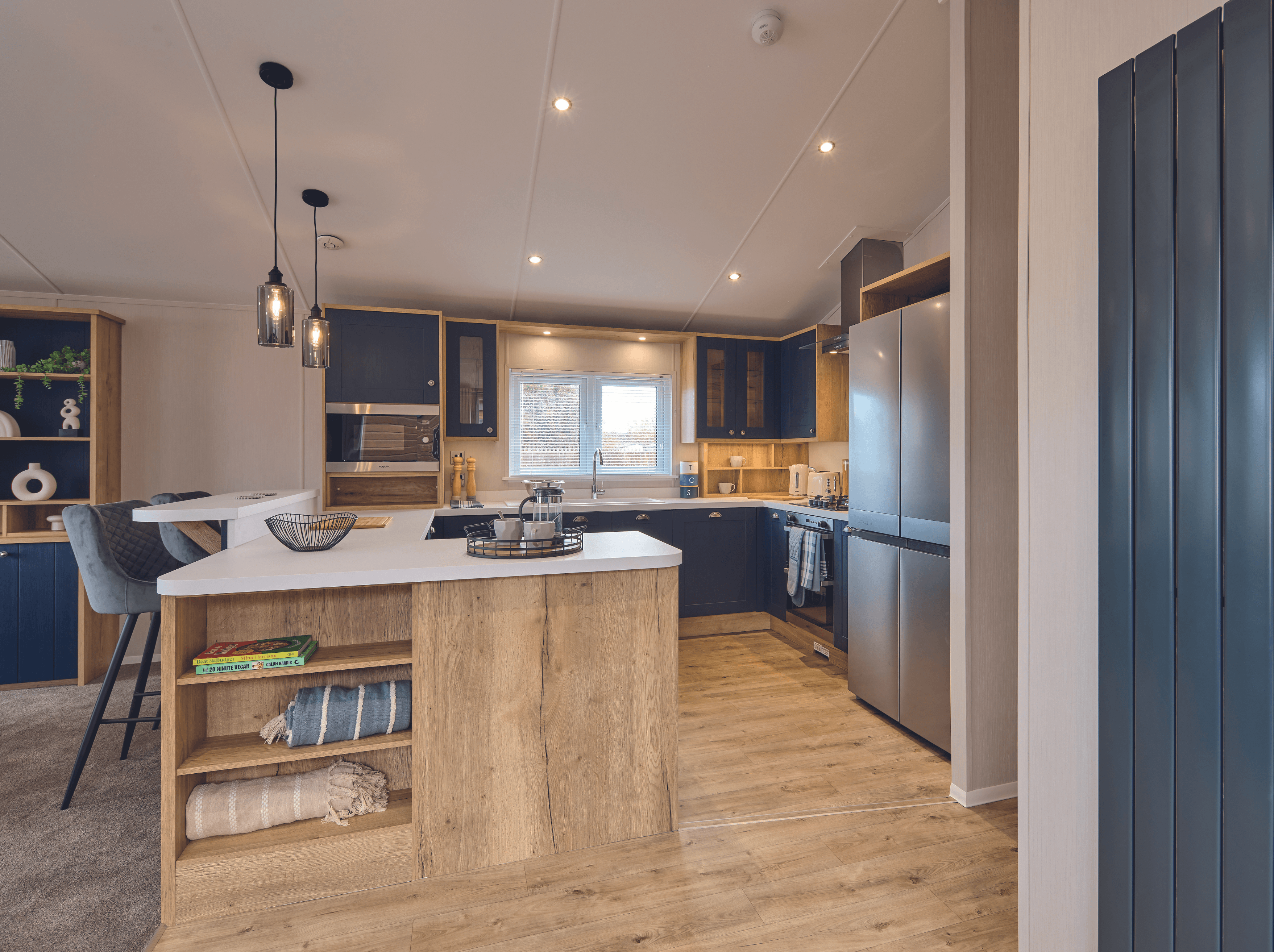 The open plan kitchen-diner of the Willerby New Holland holiday lodge. The colour scheme is dark blue and white with wooden units. The kitchen is spacious with a large fridge and there is a breakfast bar. 