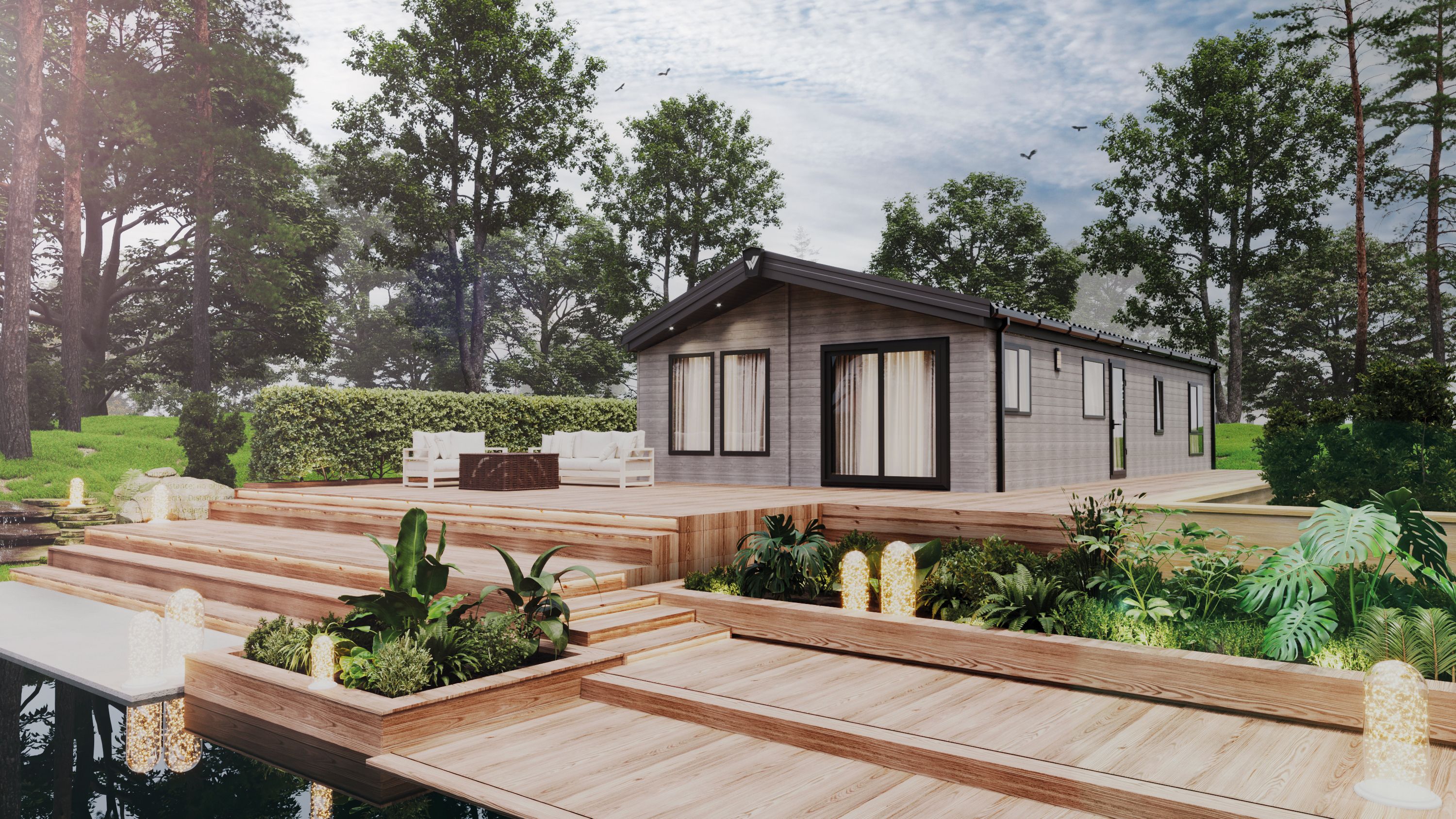 The Willerby New Holland holiday lodge surrounded by trees and plants. There is multi-level decking in front with water features. 