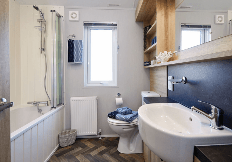 The Willerby Pinehurst bathroom has a bathtub, oak effect storage units with a deep blue splashback., matching the colour scheme of the lodge.