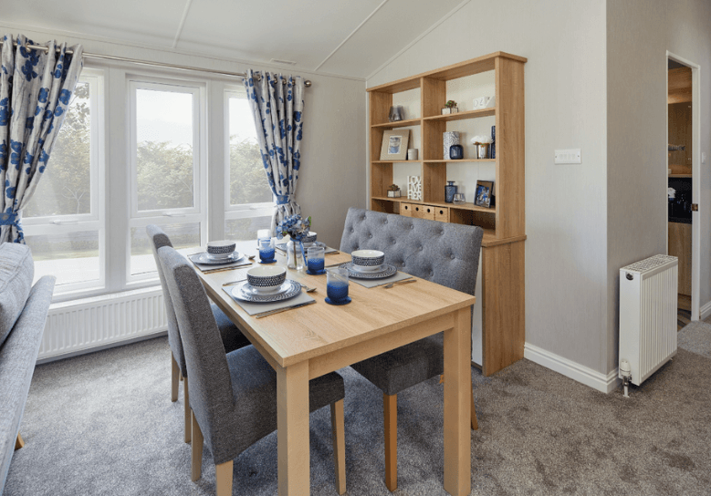 The Willerby Pinehurst dining area with grey chairs surrounding an oak effect table, with a matching ornament storage unit behind. 