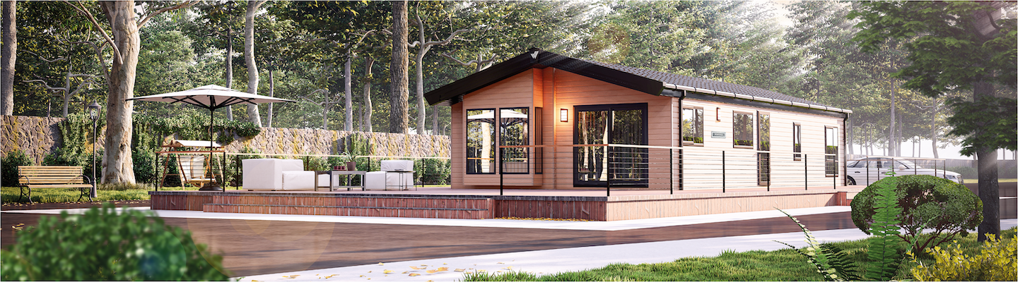 The Willerby Portland exterior in brown with brown decking sited on a grassy field with a forest behind.