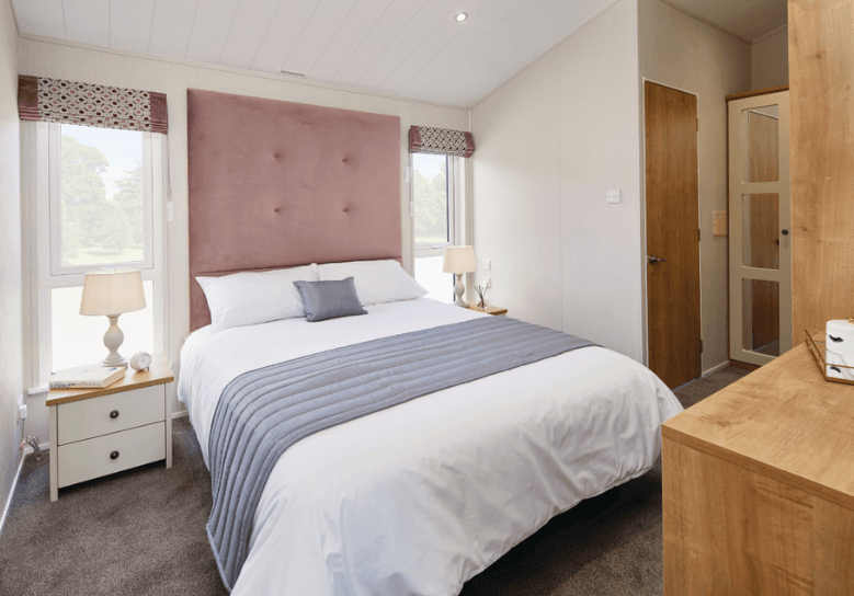 The Willerby Portland master bedroom has a tall pink upholstered headboard with oak effect bedside tables.