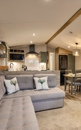 The Willerby Sierra lounge has a grey fixed L-shaped sofa with a small oak effect coffee table in the center, and a large oak effect media unit with an electric fire.