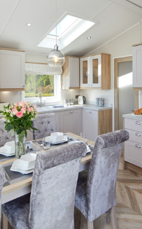 The Willerby Vogue Classique kitchen has oak effect storage units with white cupboard doors, and a luxurious oak effect and grey dining table with grey dining chairs surrounding.