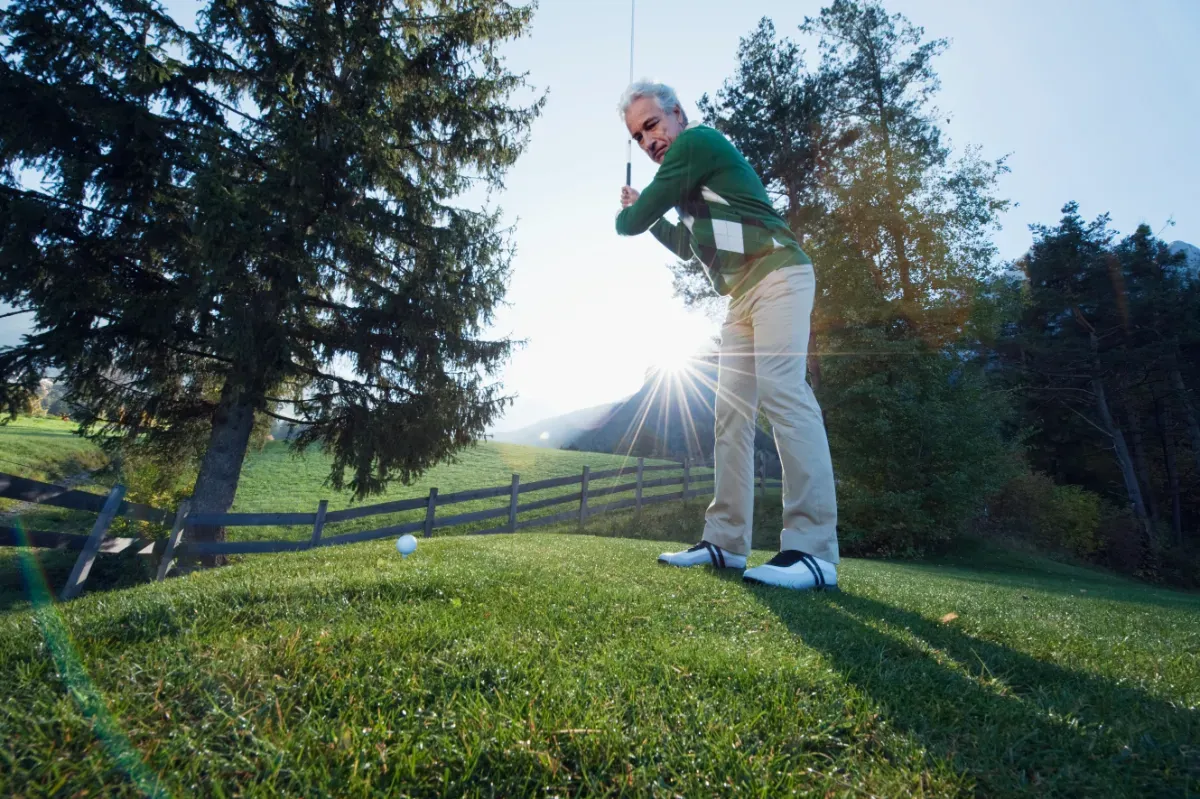 A beginner golfer takes a shot on a golf course in the early morning light. 