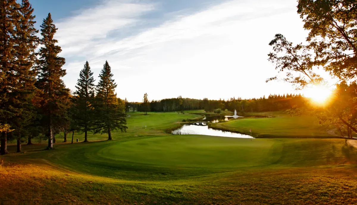 The sun rises over a scenic golf course with water features and trees.