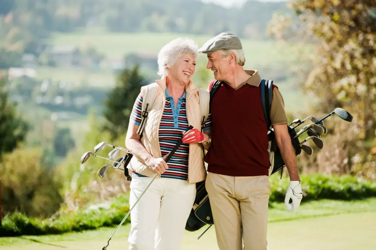  Older couple enjoying a round of golf on a sunny day, smiling and laughing. 