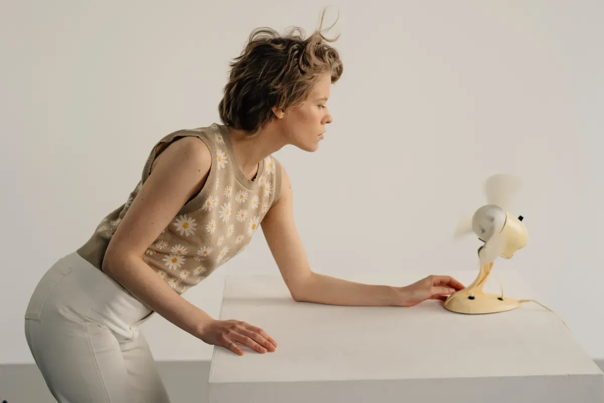 A woman trying to keep cool using a small desk fan. 