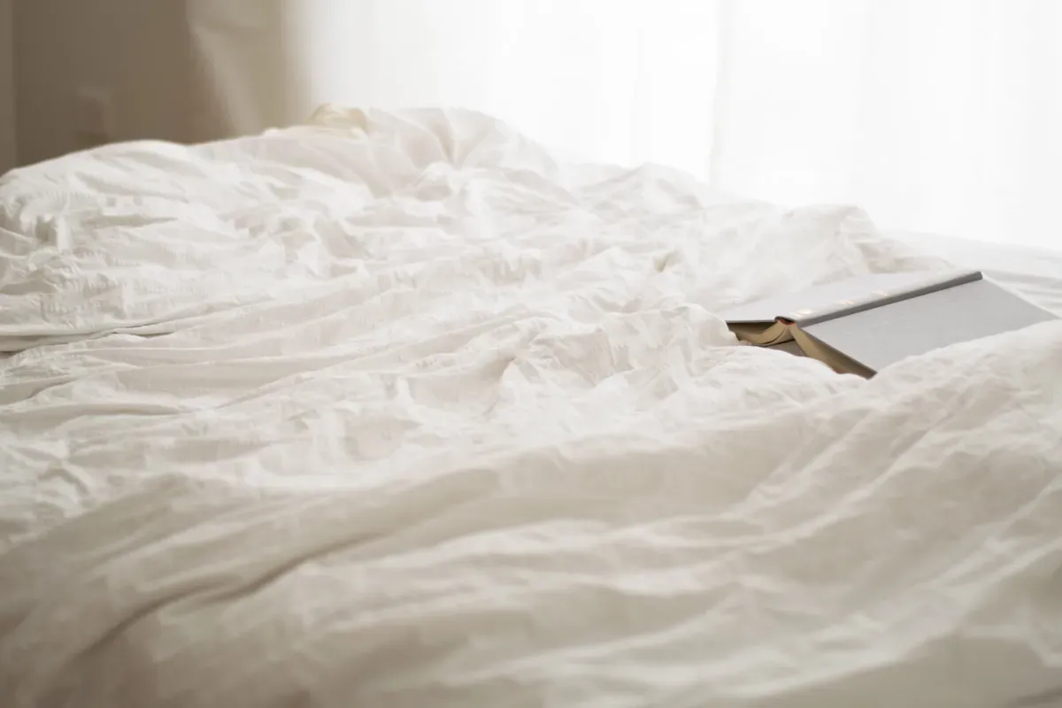 Cool white Egyptian sheets on a static caravan bed in summer with a book on top of them. 