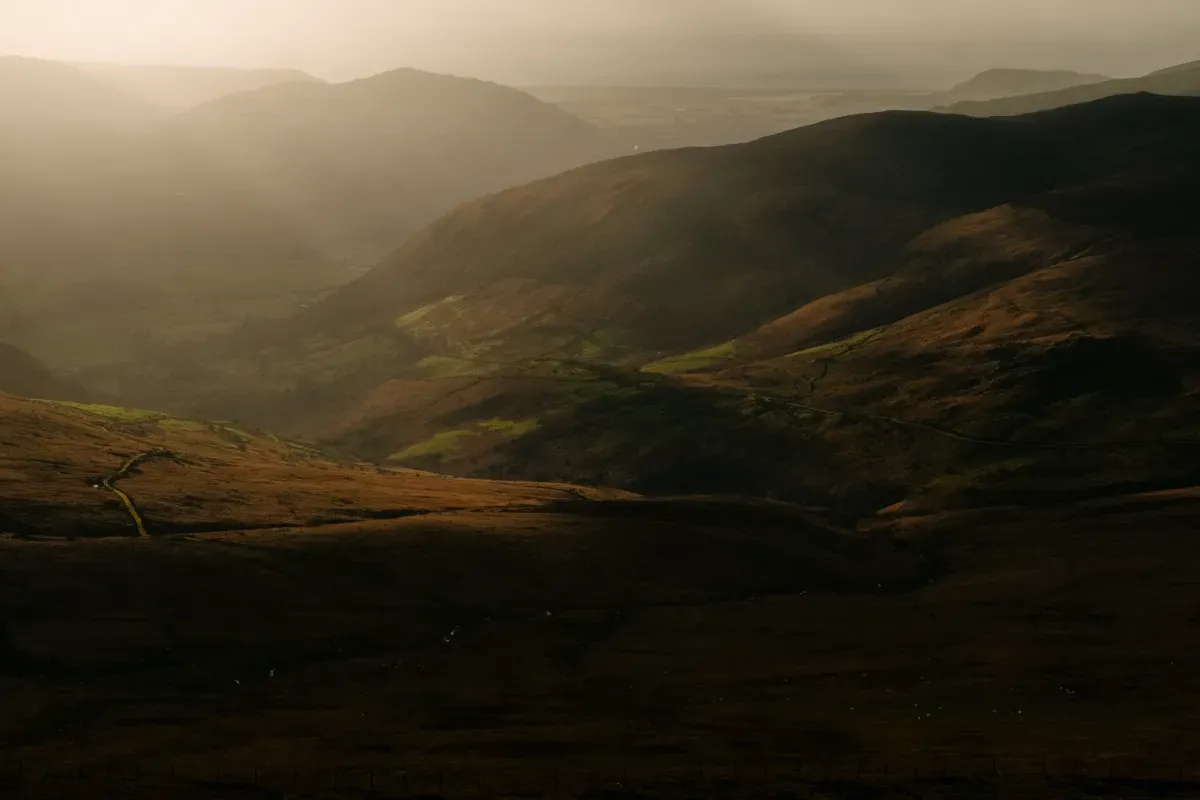 View from Cadair Idris with the sun low in the sky casting golden light over nearby hills.