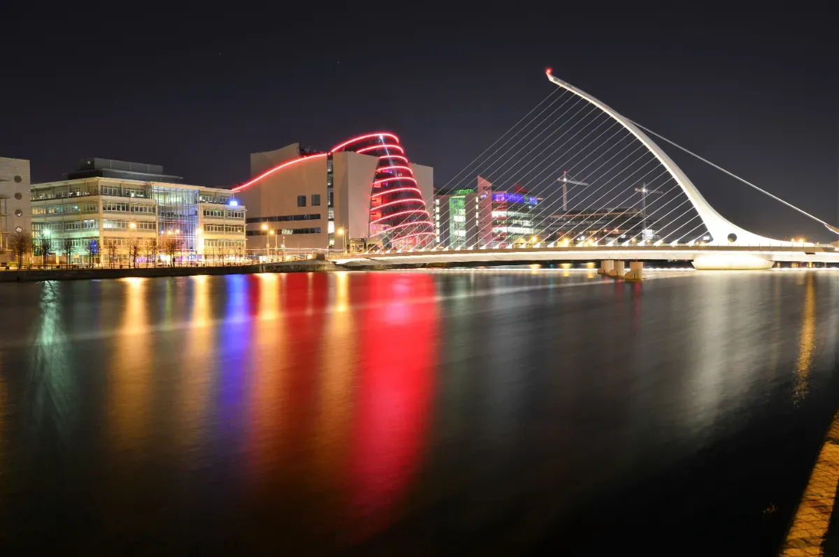 A view of Dublin at night, showing the Samuel Beckett Bridge and Dublin Convention Centre reflected in the River Liffey